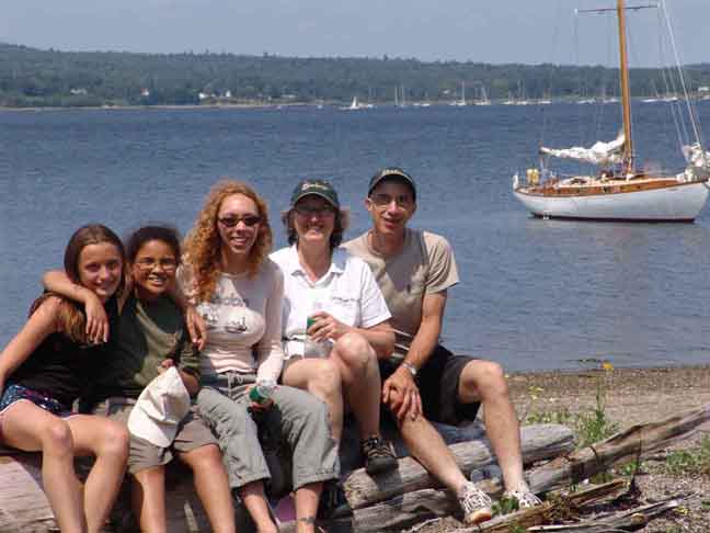 family of 5 on the beach with viva at anchor in the background